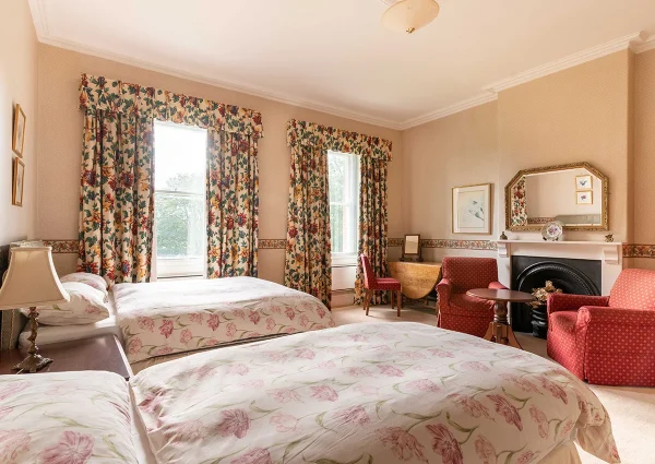 Two double beds and two red armchairs in the Laburnum bedroom. There is also a folding desk and chair in the far corner.